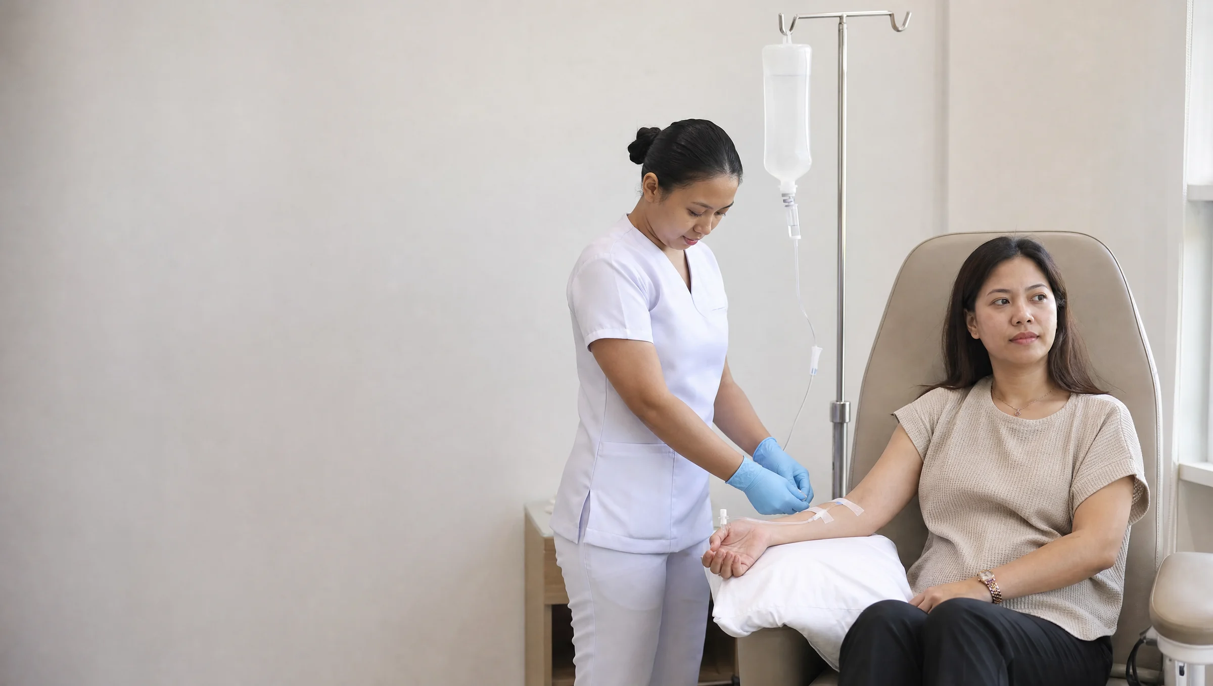 An intravenous drip bag and line beside a treatment chair in a bright clinic room
