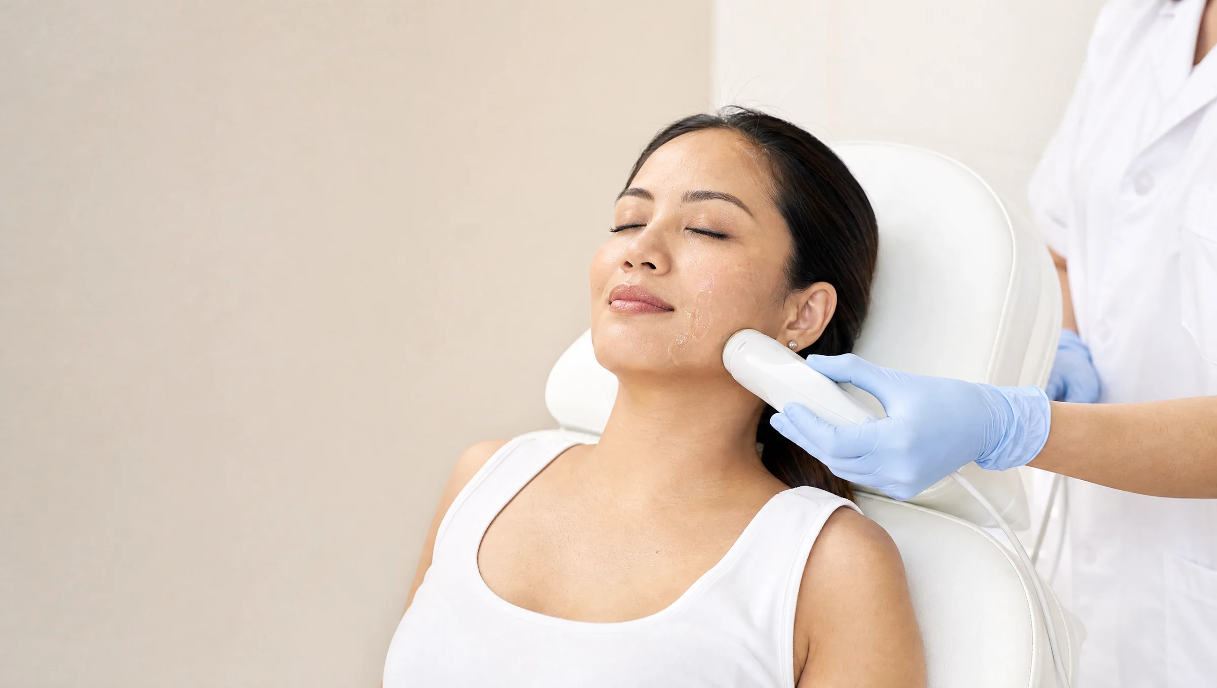 A practitioner treating a patient's jawline in a bright clinic room